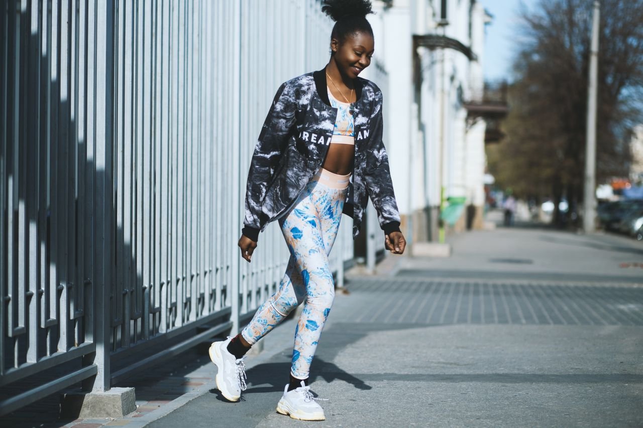 Stylish woman in sportswear walking on a sunny urban sidewalk, embracing fitness and fashion.