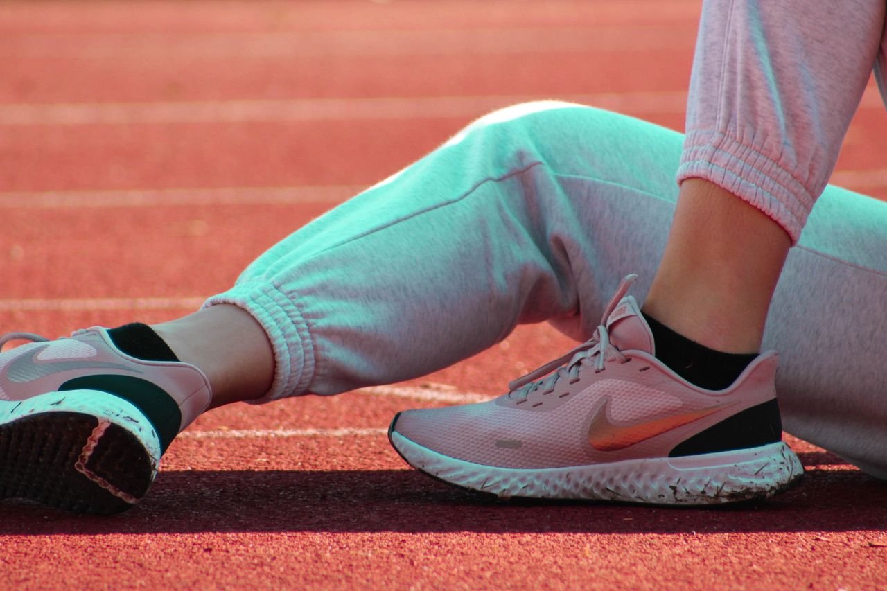 Close-up of athlete resting on track, showcasing pink sports shoes in warm sunlight.