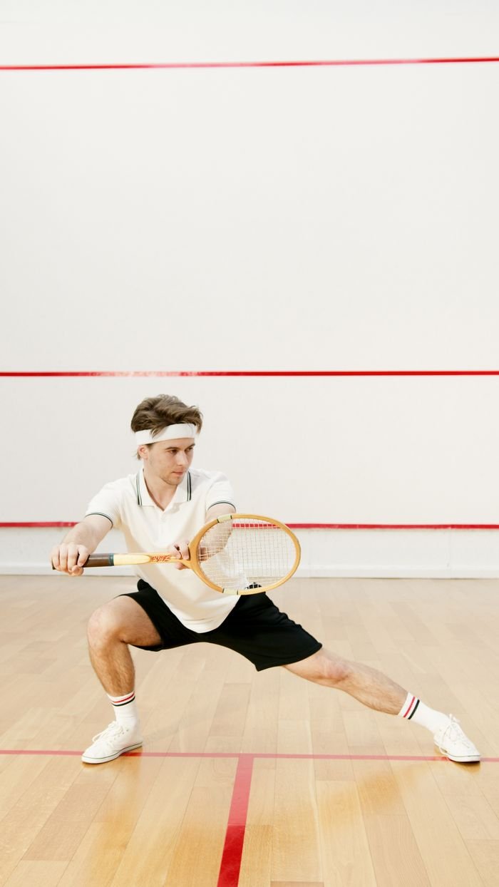 Male athlete playing squash, showcasing skill and agility indoors on a wooden court.